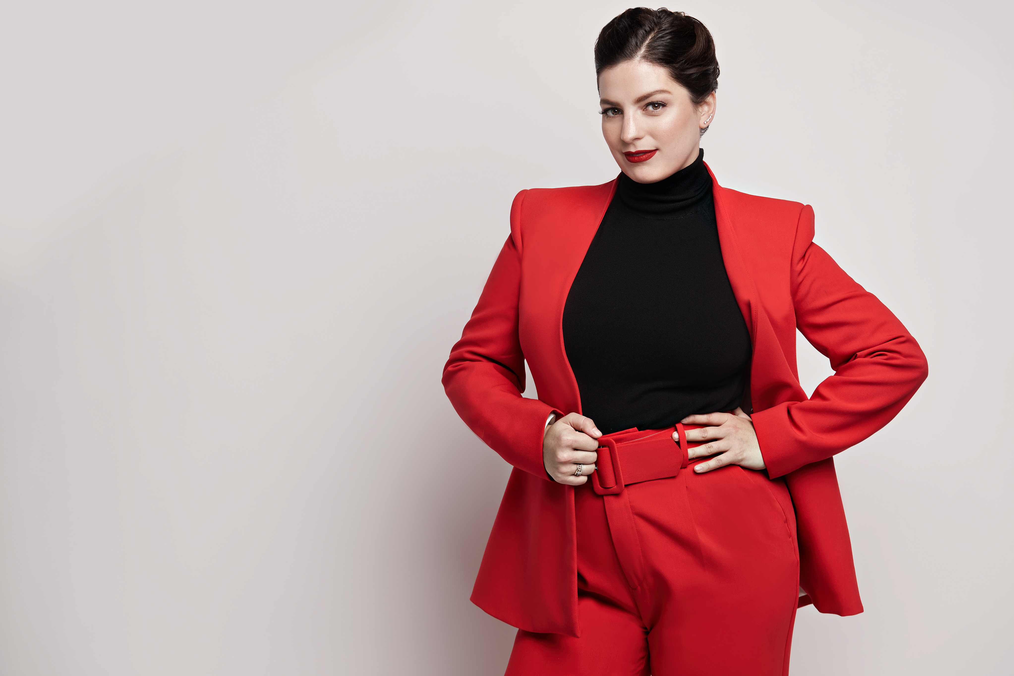 argentinian italian woman with dark hair slicked back wearing a red suit with hands on her hips