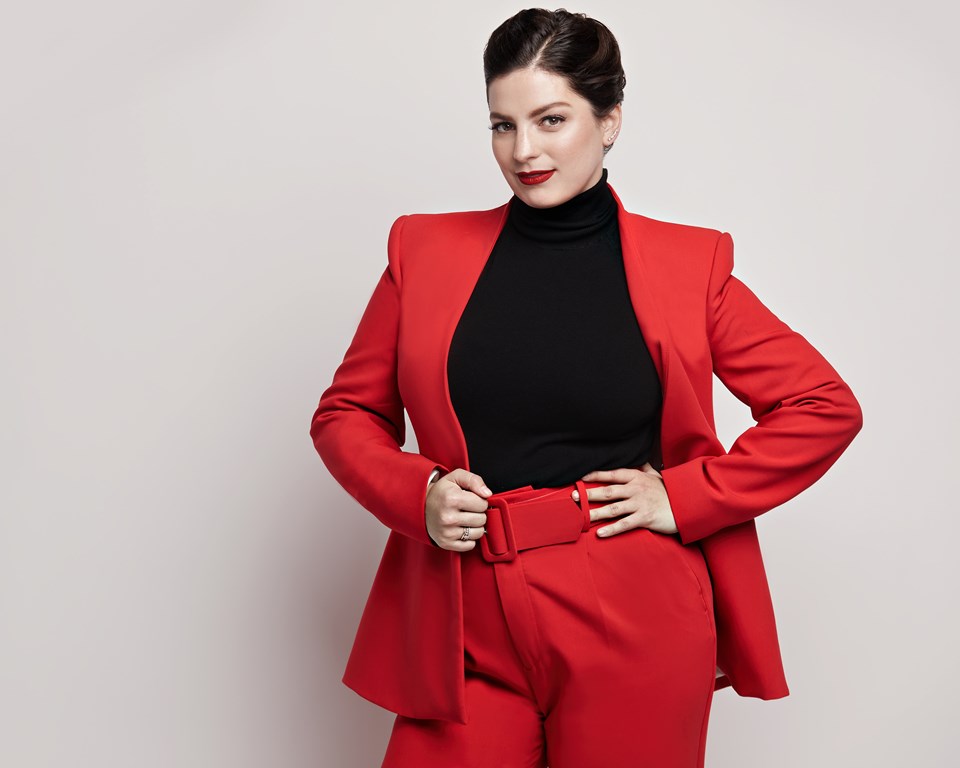 argentinian italian woman with dark hair slicked back wearing a red suit with hands on her hips
