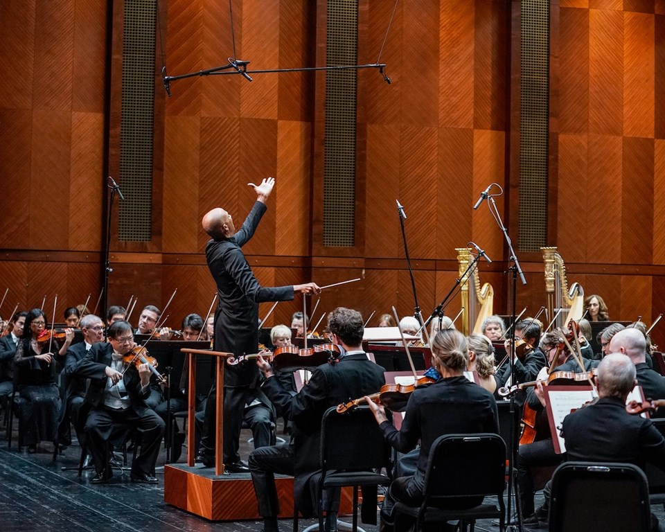 black conductor with arm raised high above orchestra