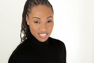 black woman long braids pulled back into a pony tail, wearing a black turtle neck and an open mouth smile