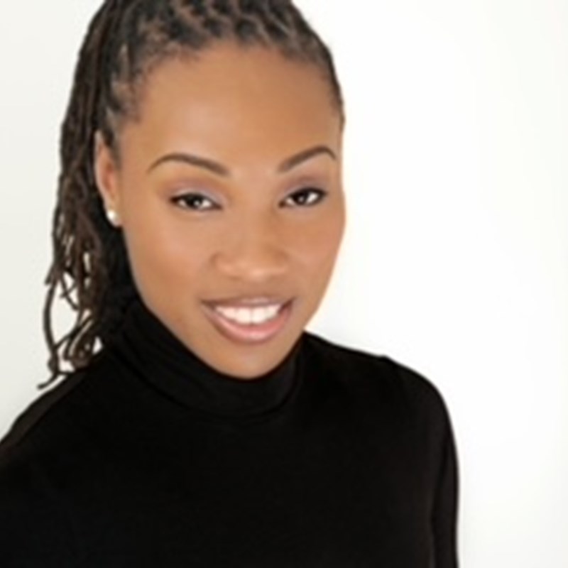 black woman long braids pulled back into a pony tail, wearing a black turtle neck and an open mouth smile