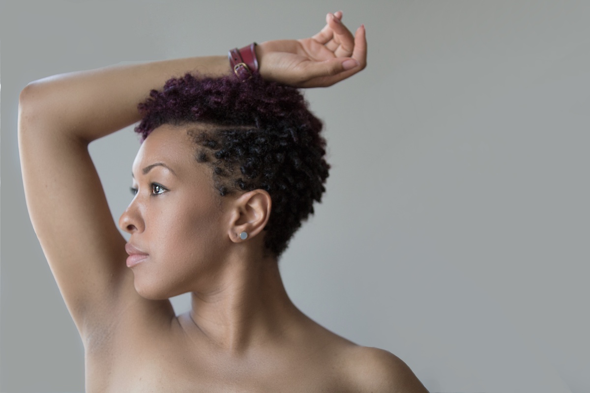 black woman with short hair look to the side with hand resting on head