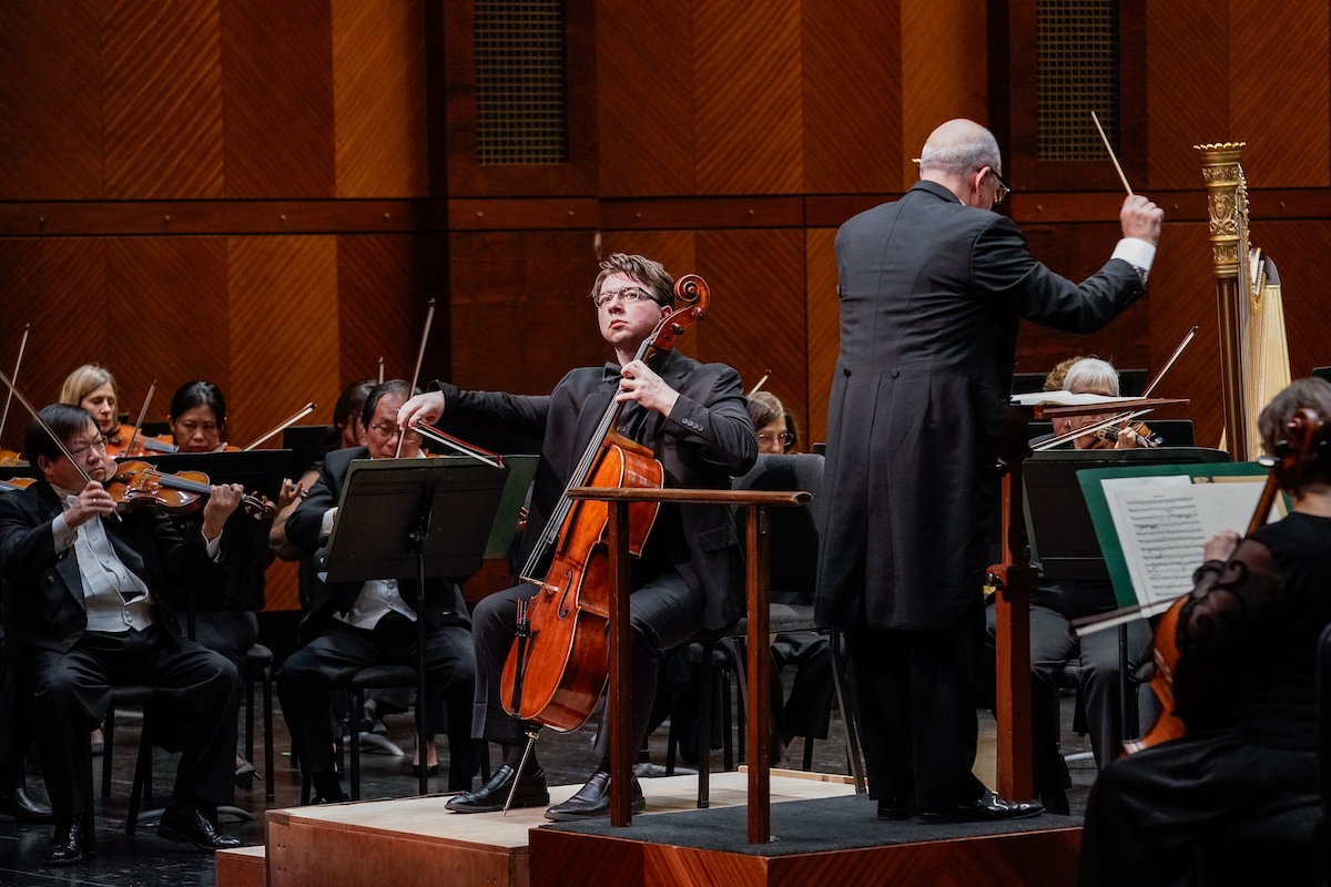 White man with medium length hair playing cello solo 