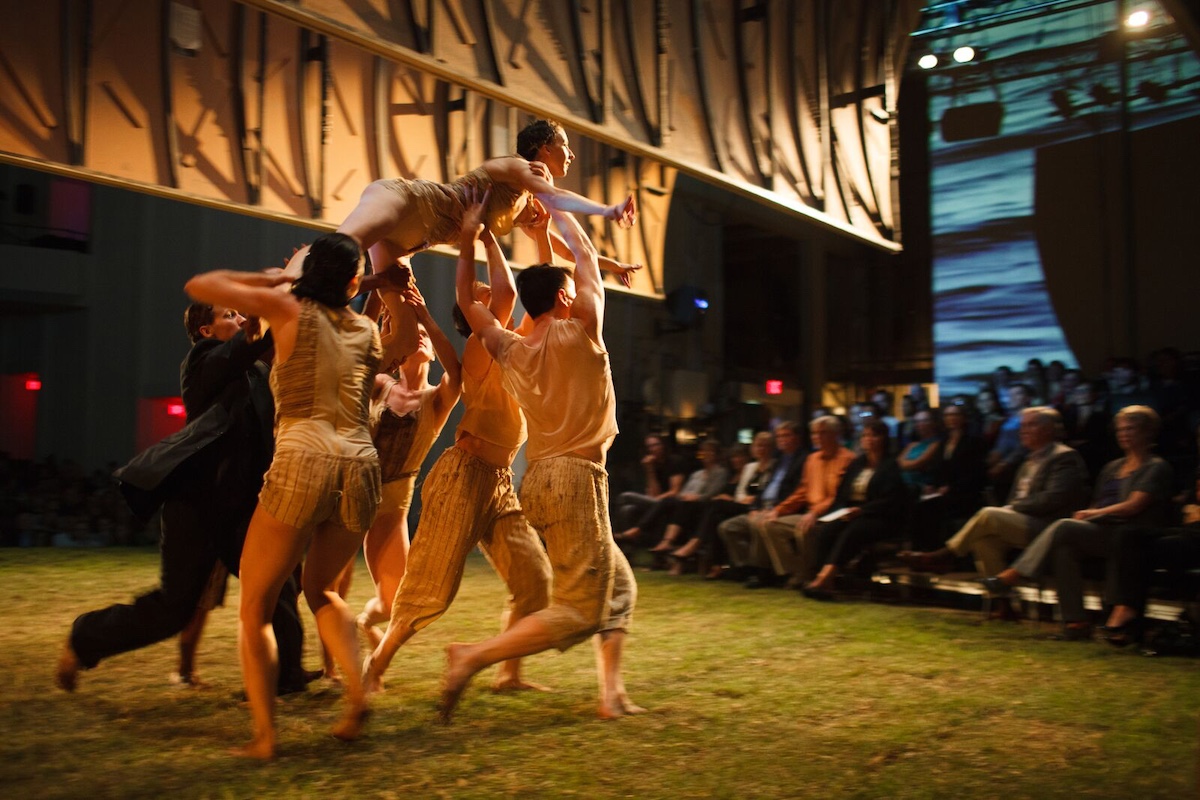 dancers holding woman up over a grass stage in front of an audience