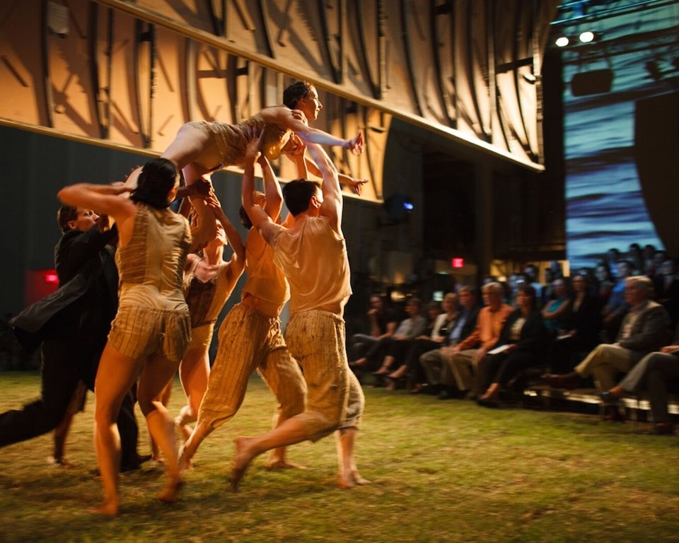 dancers holding woman up over a grass stage in front of an audience