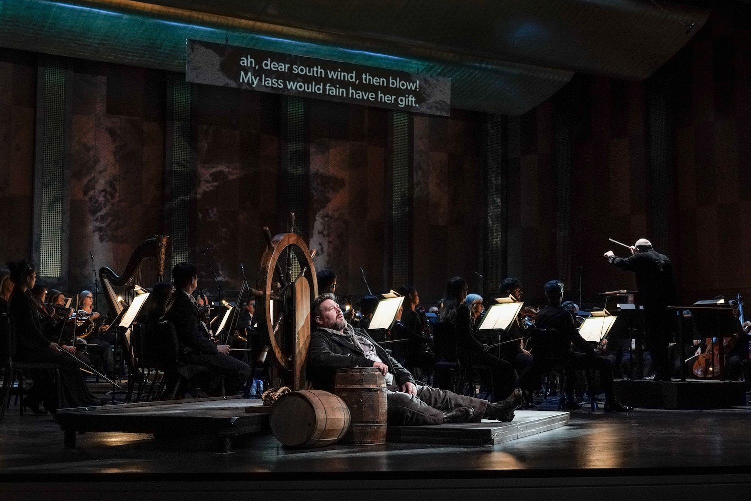 man opera singer leaning on ship wheel in front of orchestra