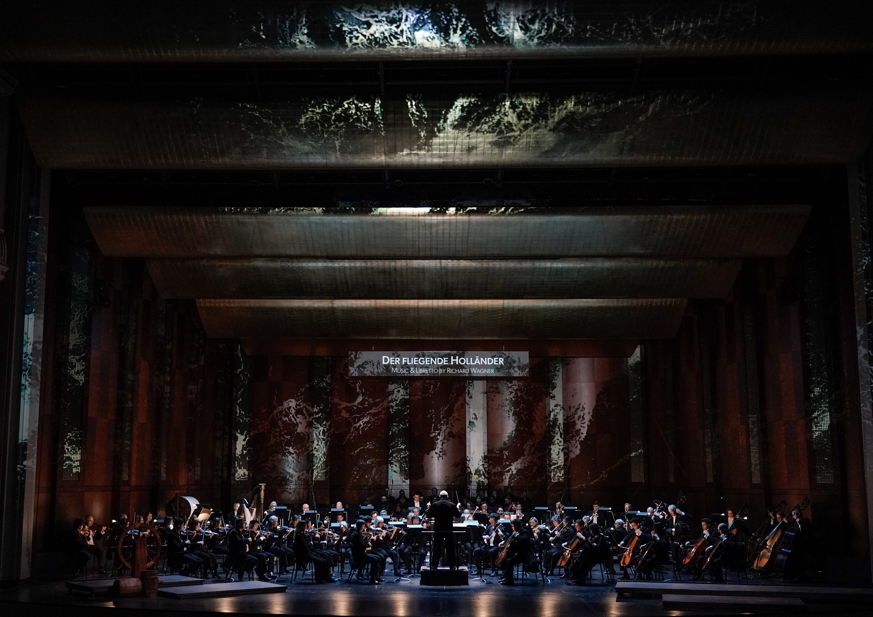 full symphony orchestra on stage with conductor with projections of water and The Flying Dutchman supertitle
