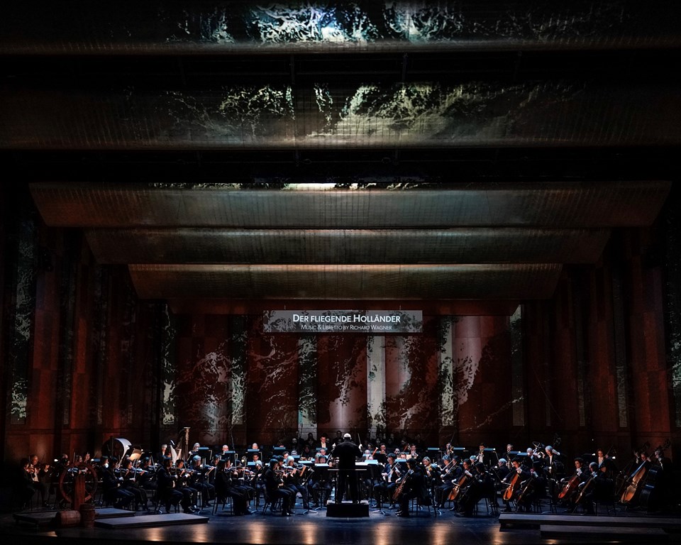 full symphony orchestra on stage with conductor with projections of water and The Flying Dutchman supertitle