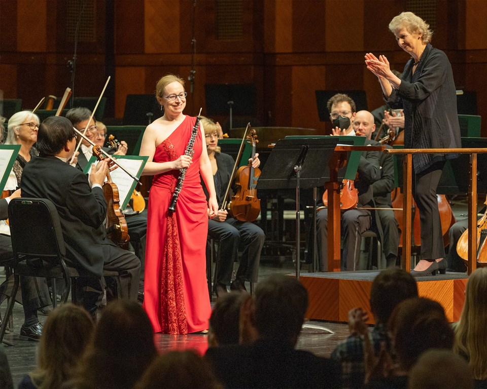 Female oboe player in red dress smiling on stage with conductor clapping for her