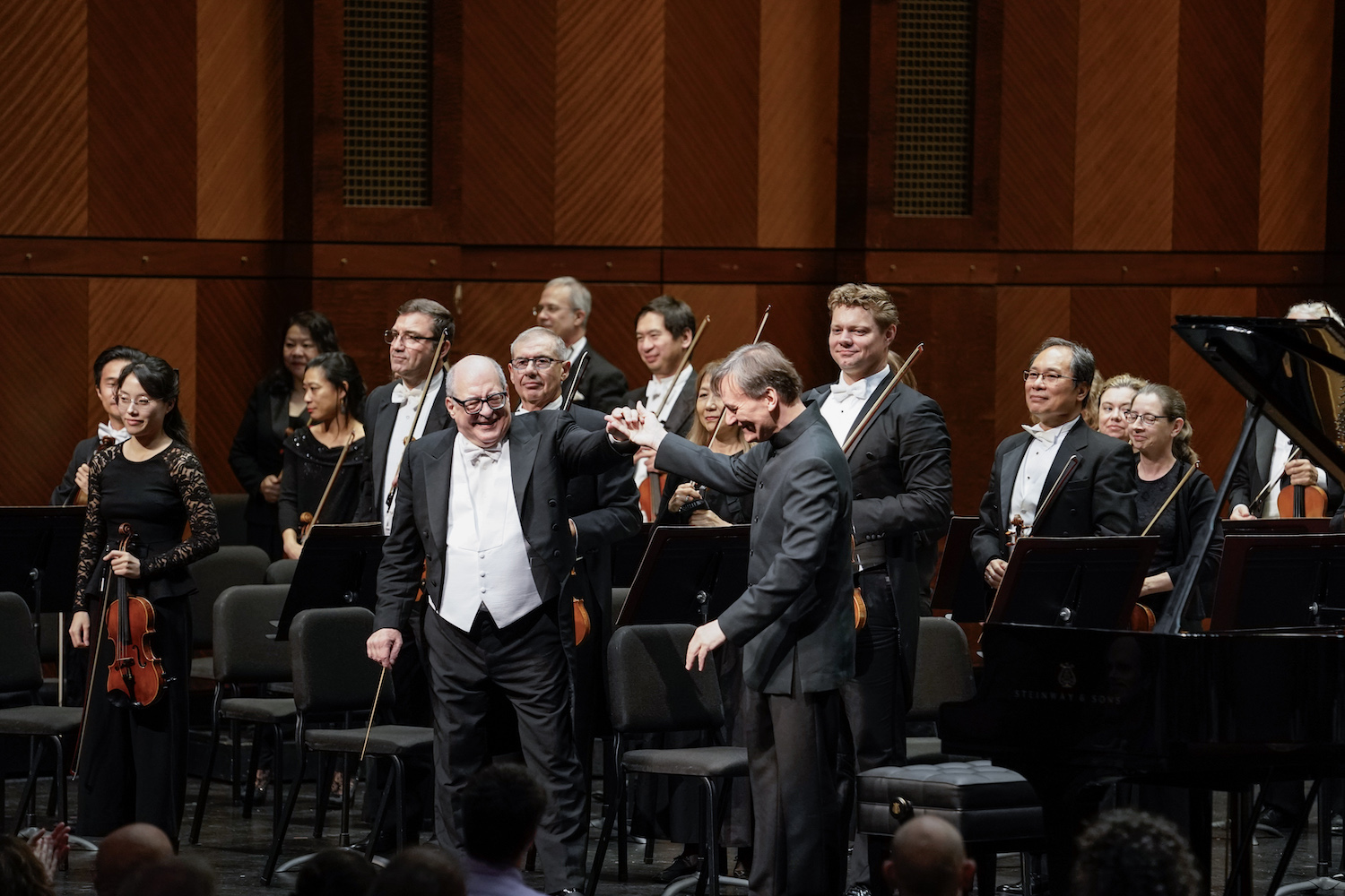 Conductor and pianist smiling and standing on stage in front of orchestra