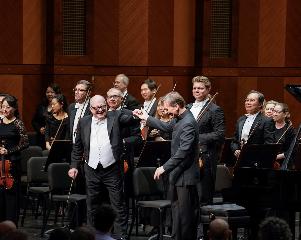 Conductor and pianist smiling and standing on stage in front of orchestra