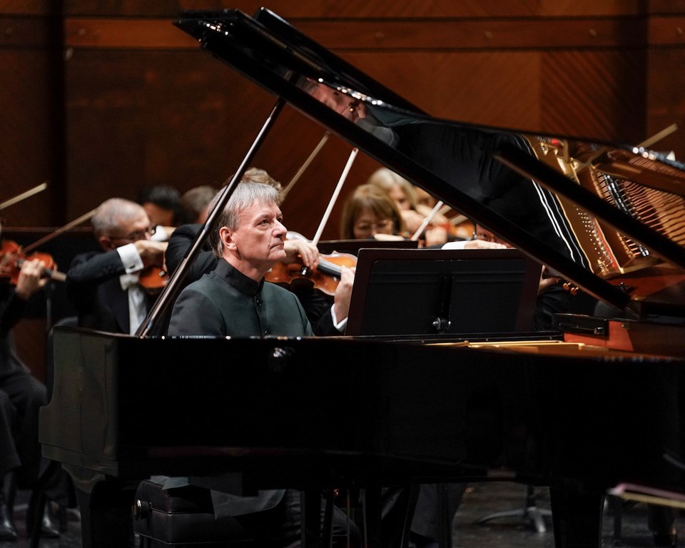 Man with grey hair and black shirt performing a grand piano