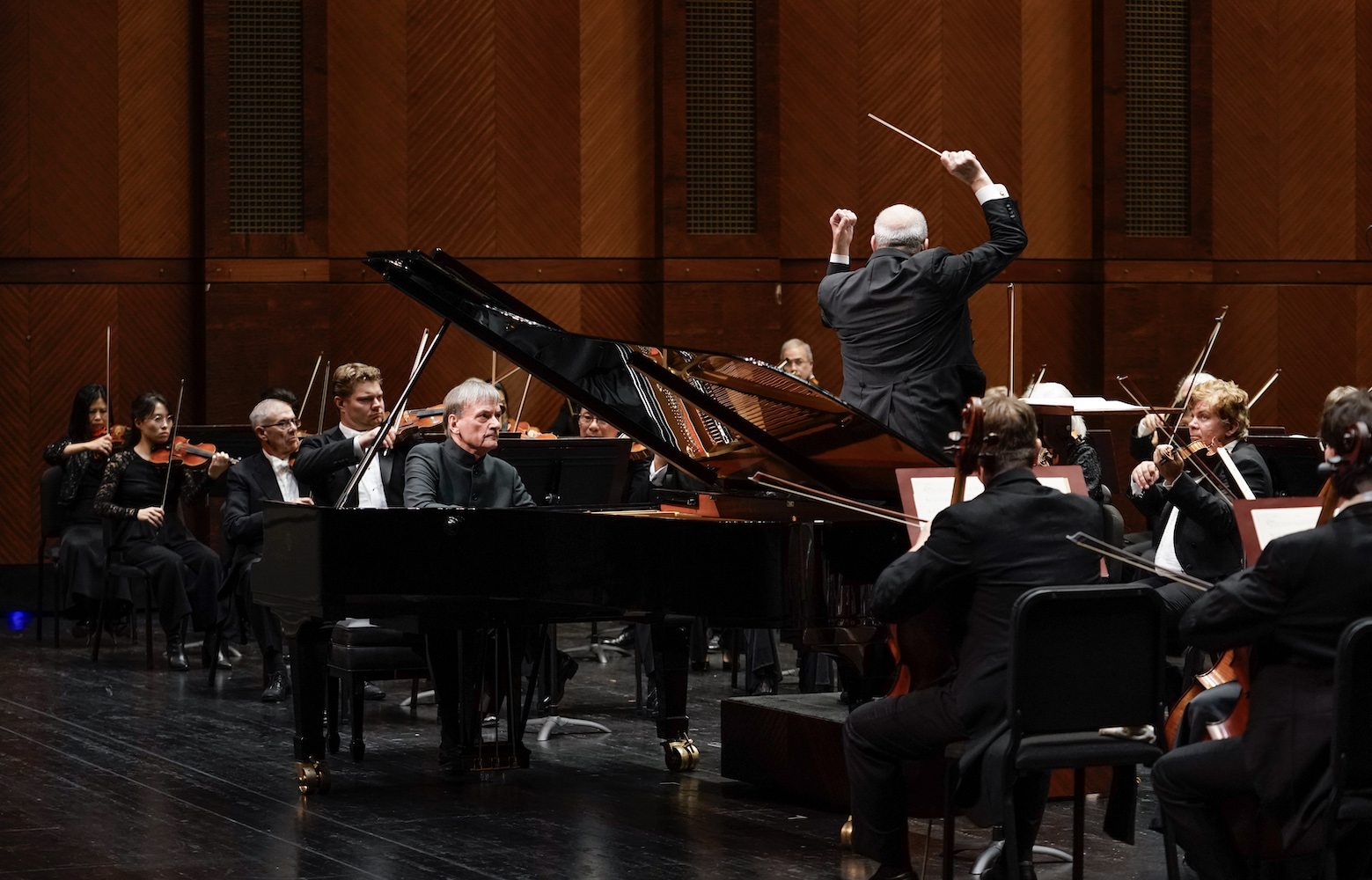 Pianist performing a grand piano on stage with a conductor with his arms up