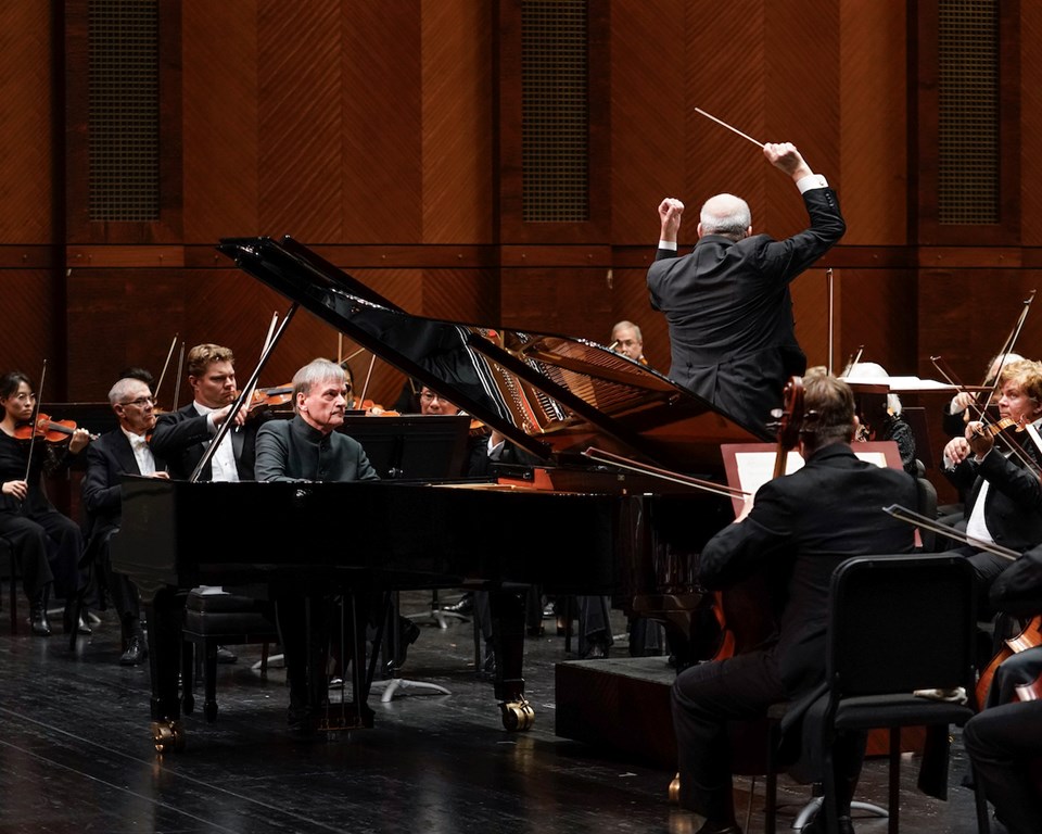 Pianist performing a grand piano on stage with a conductor with his arms up