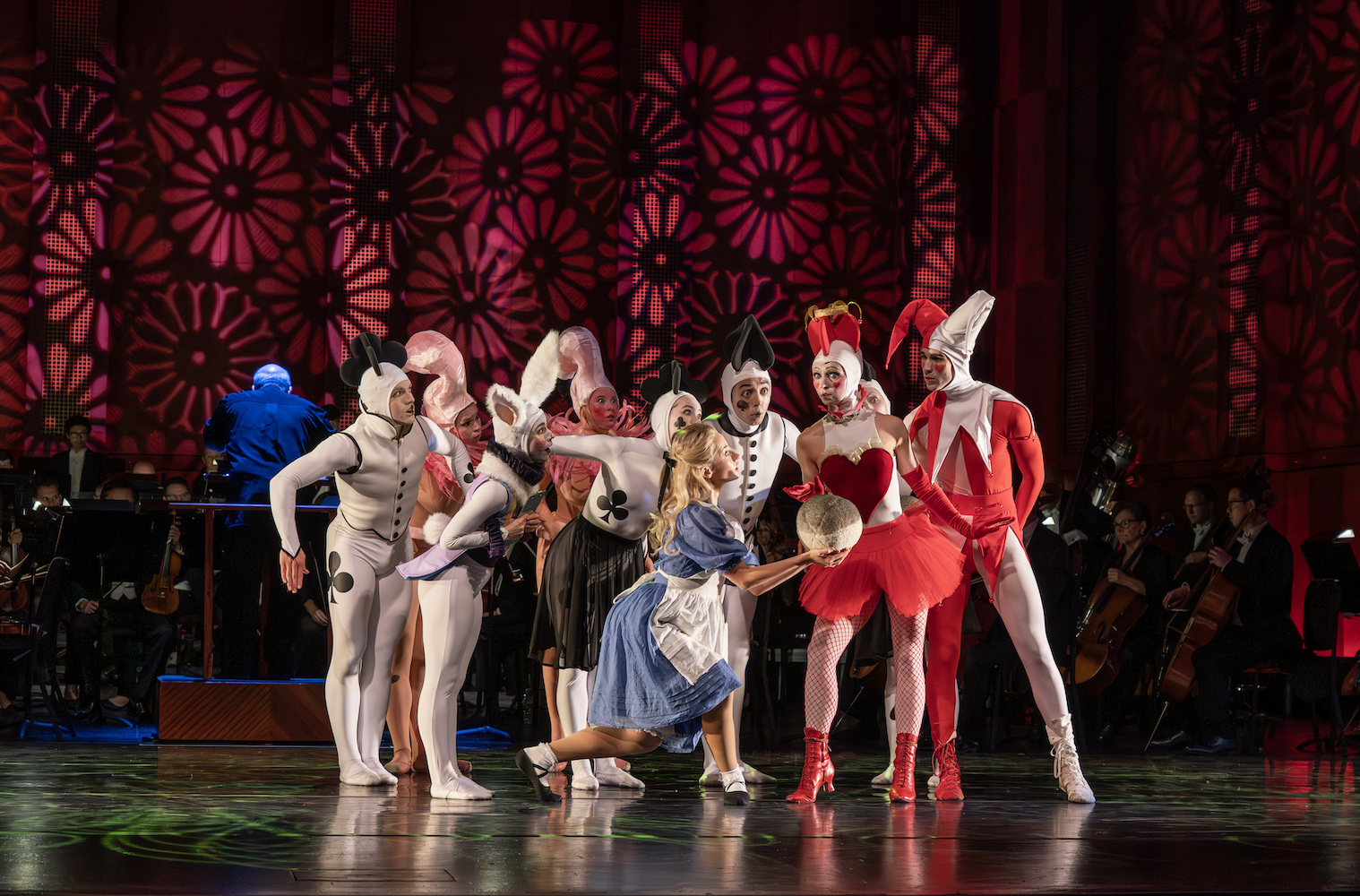 Alice in Wonderland dancers standing in a group on stage in front of an orchestra