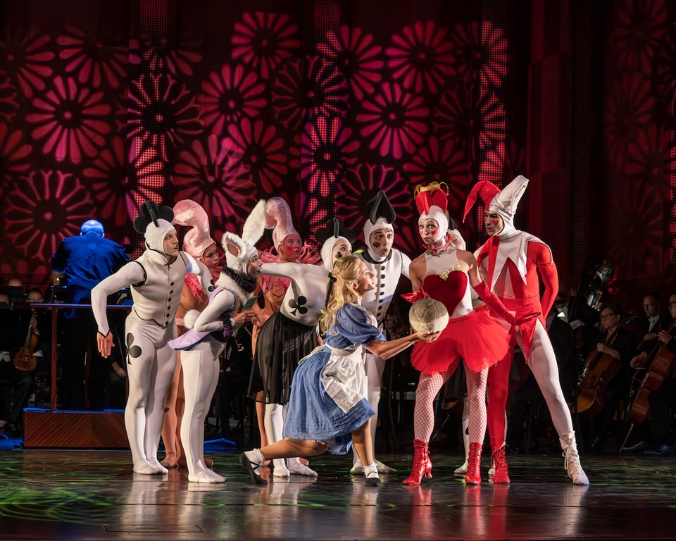 Alice in Wonderland dancers standing in a group on stage in front of an orchestra