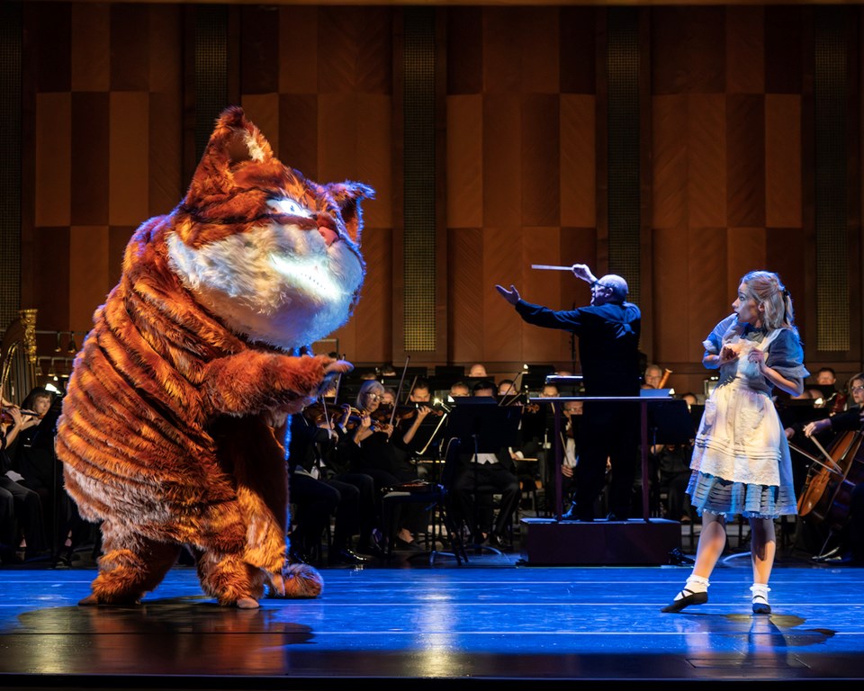 Large orange cat and dancer dressed like Alice in Wonderland on stage in front of orchestra