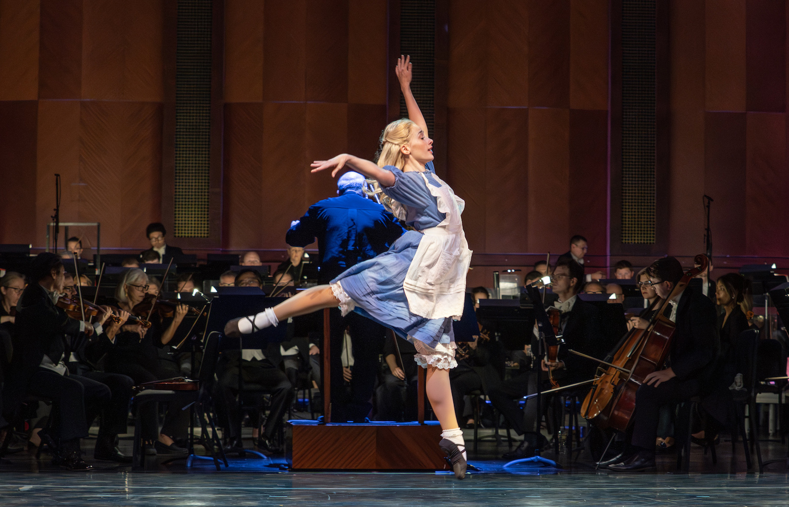 Female ballet dancer jumping in front of symphony orchestra on stage