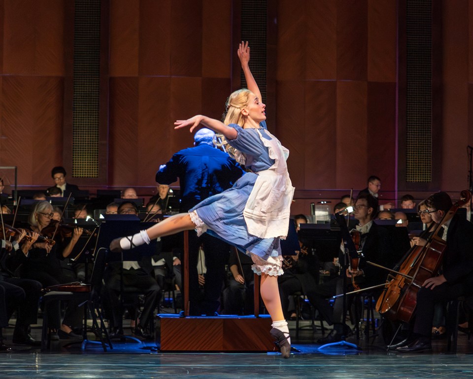Female ballet dancer jumping in front of symphony orchestra on stage